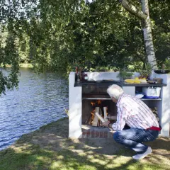 Man tänder en brasa vid en murad grillplats vid en sjö.