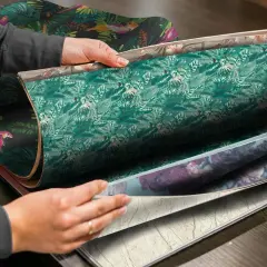 Händer bläddrar i en tapetbok med djungelmotiv och blomstermönster. Perfekt för att välja non woven lim till papperstapet.