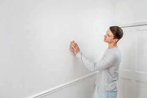 Man känner på en vit vägg, redo att ta bort tapet för att fräscha upp rummet.
