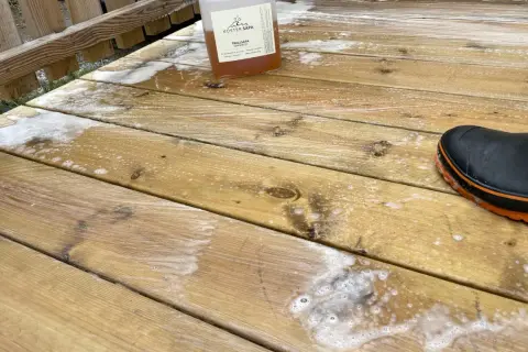 En flaska såpa står på en altan med såpskum. En svart stövel med orange kant syns i nedre högra hörnet.