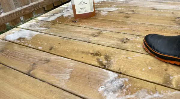 En flaska såpa står på en altan med såpskum. En svart stövel med orange kant syns i nedre högra hörnet.