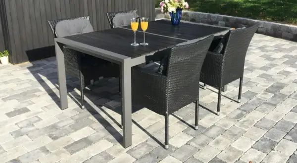 En vacker stenlagd uteplats med ett mörkt matbord och stolar, perfekt för inspiration. Två glas med apelsinjuice står redo.