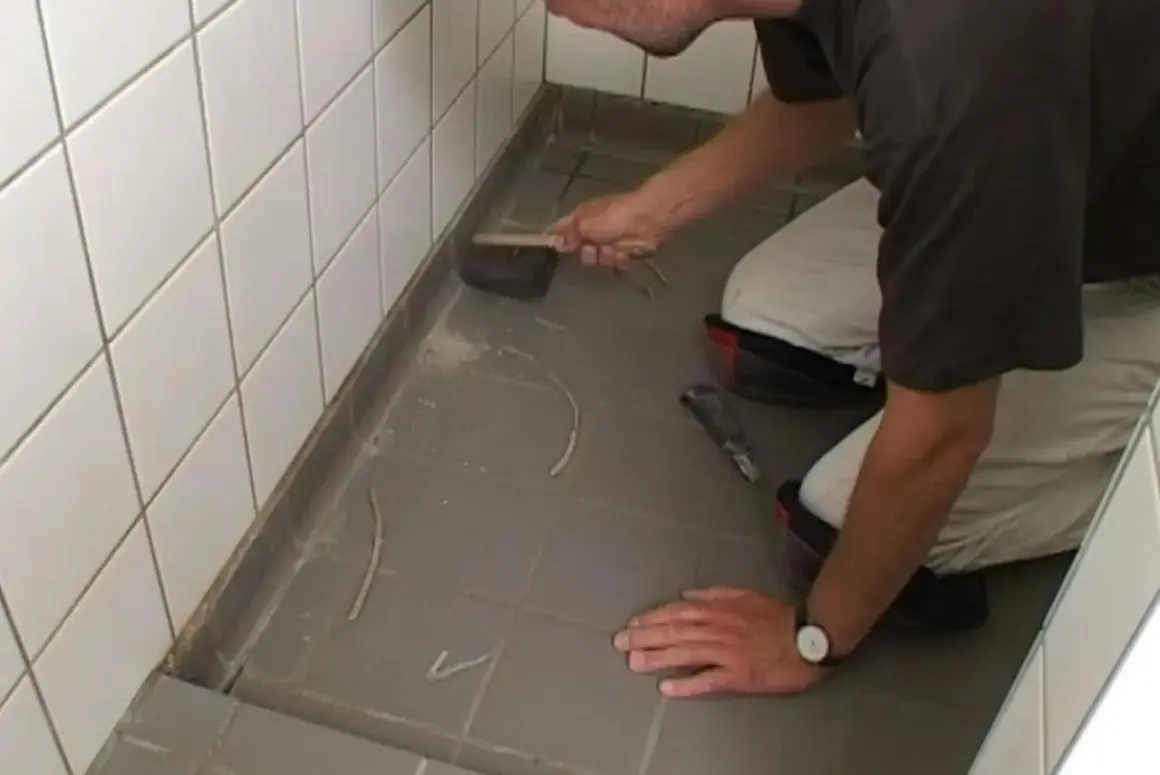 Man knäböjer och använder en borste för att ta bort silikonfog runt en dusch.