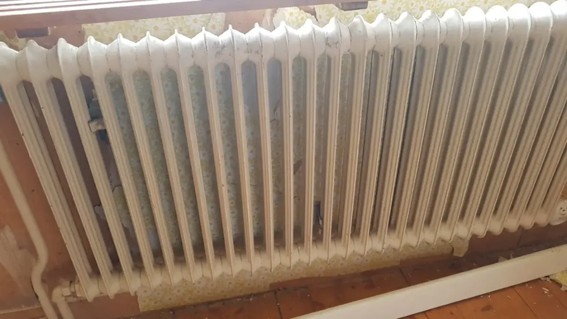 Gammal vit element med blommig tapet bakom. Kanske dags att ta bort elementet och tapeten för en renovering.
