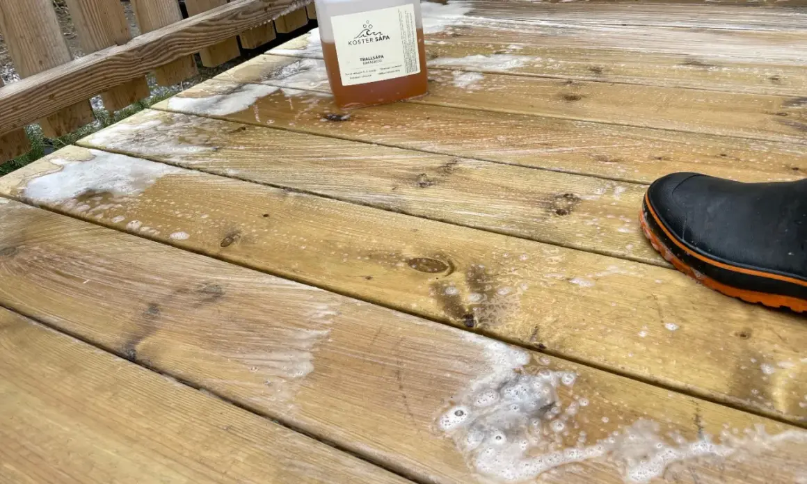 En flaska såpa står på en altan med såpskum. En svart stövel med orange kant syns i nedre högra hörnet.