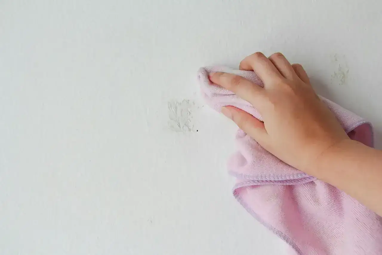 Hand med rosa trasa som f&ouml;rs&ouml;ker ta bort klister p&aring; m&aring;lad yta.