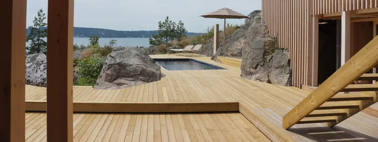 En stor altan i tr&auml; med en pool och solstolar, omgiven av klippor och med utsikt &ouml;ver vattnet. Perfekt f&ouml;r en fris trall.