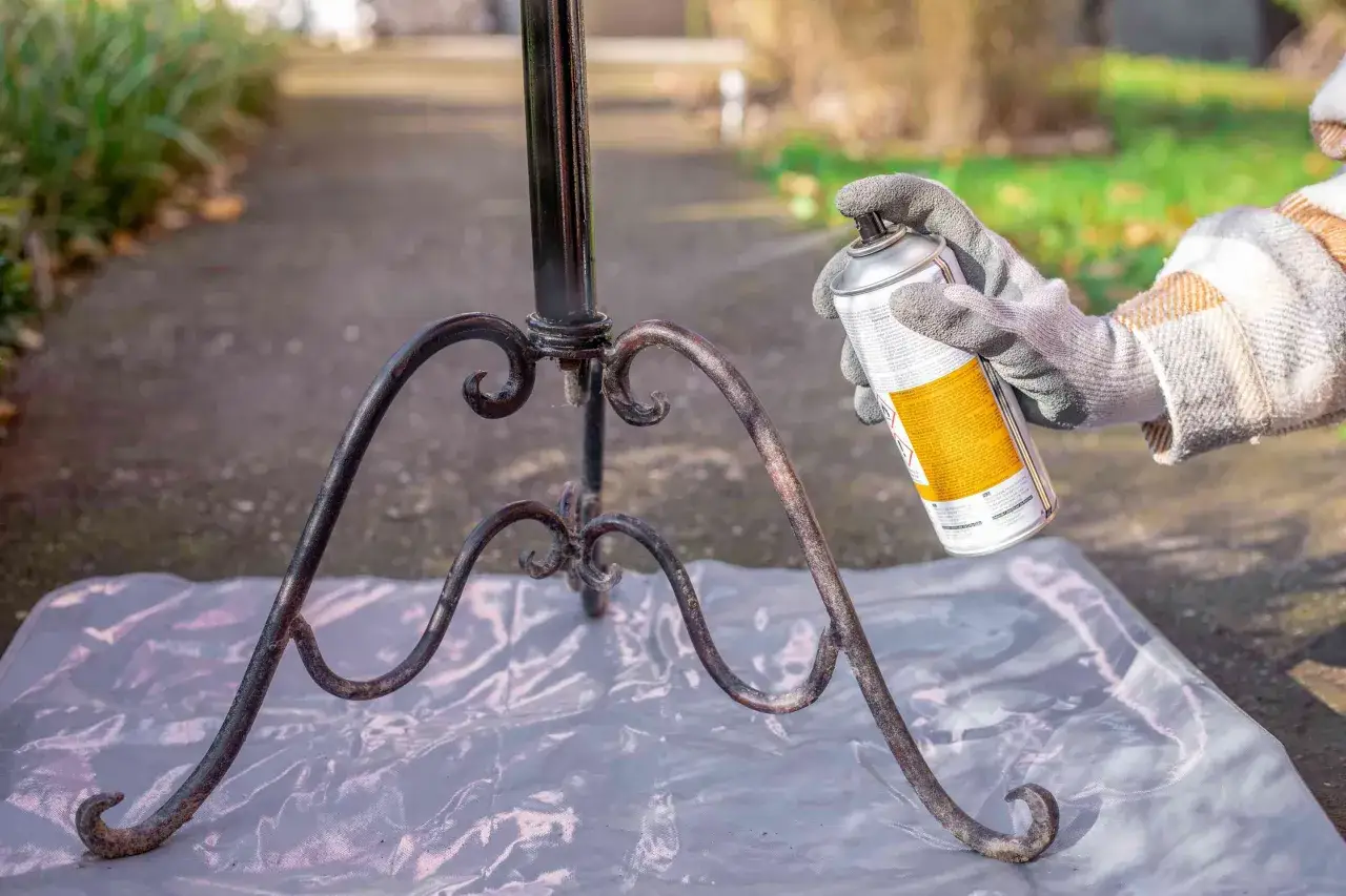 En hand med handske sprayar en rostig metallst&auml;llning utomhus.