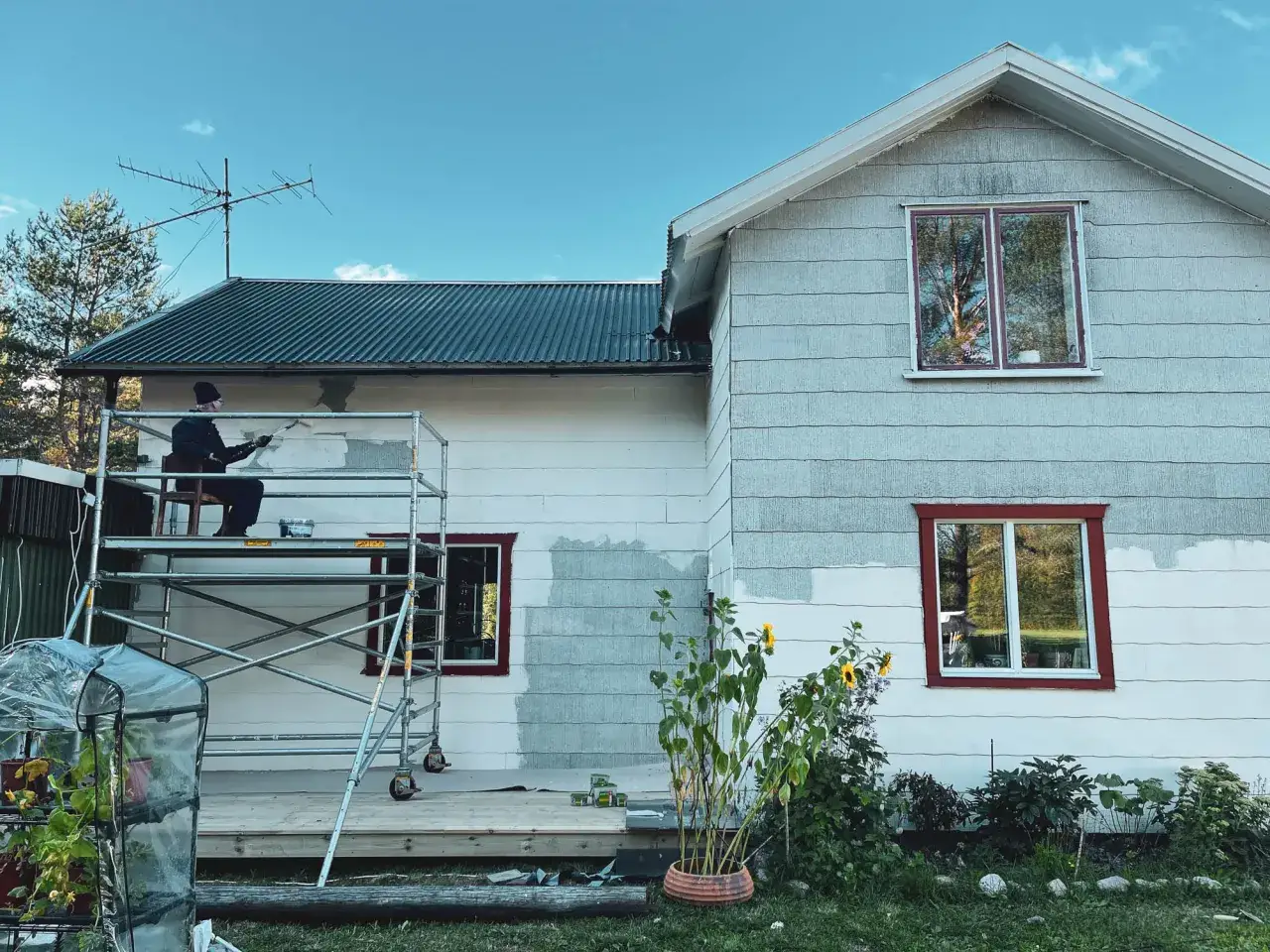 Person m&aring;lar om husets eternit fasad fr&aring;n st&auml;llning.