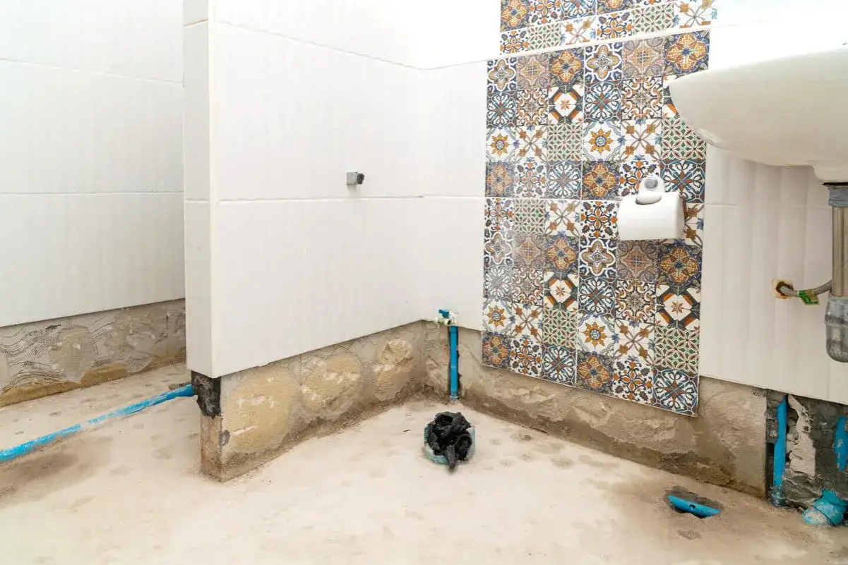 Renovering av badrum. Väggarna är kaklade, men golvet och nedre delen av väggarna är oklara. En toalettrulle hänger på en vägg med mönstrat kakel. Kanske dags att måla våtrumsmatta?