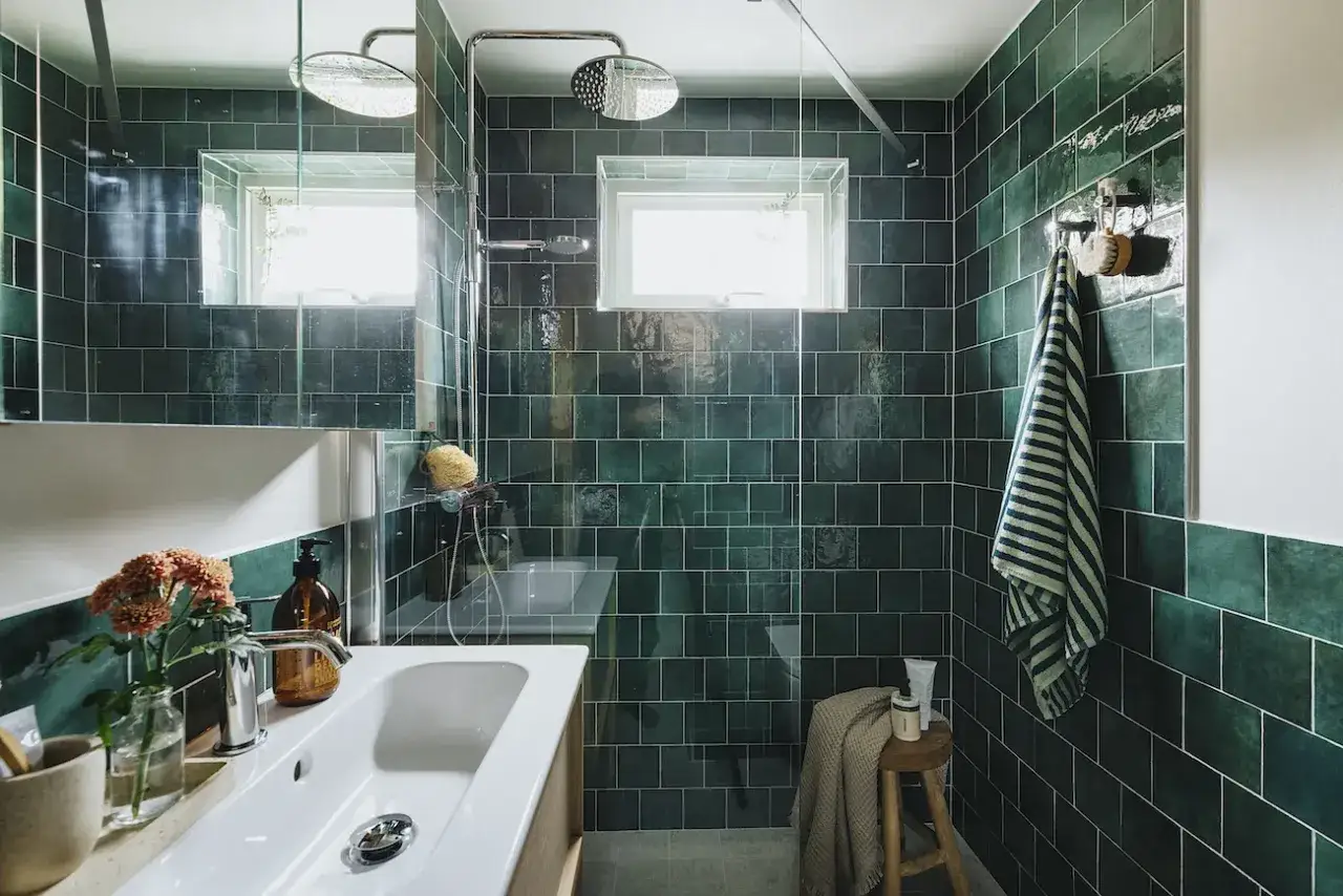 Ett modernt badrum med mörkgröna kakelplattor, en vit kommod med handfat och en duschhörna. Perfekt för en renovering badrum.