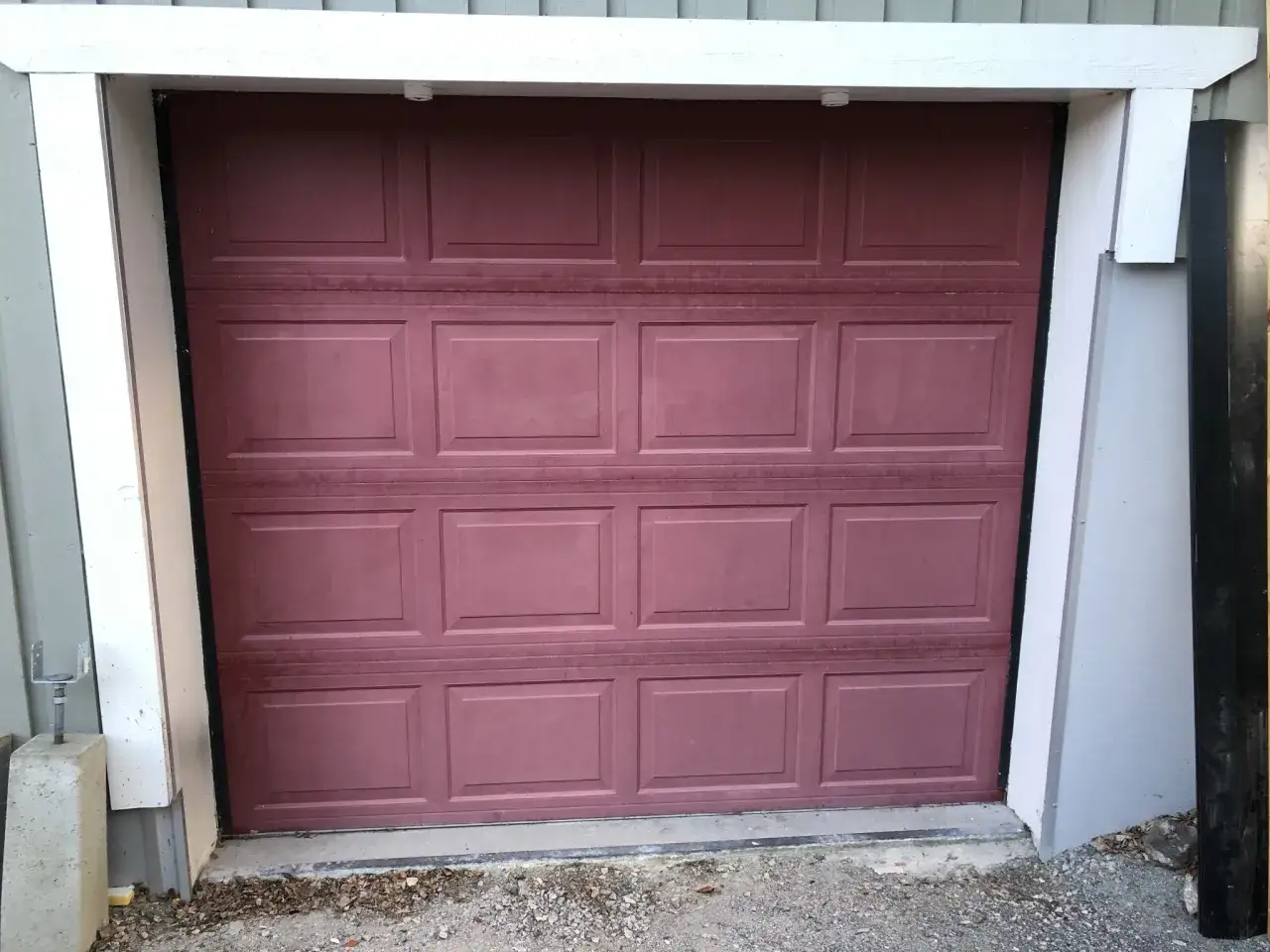 En m&ouml;rkr&ouml;d garageport med paneler, redo att m&aring;la om f&ouml;r ett fr&auml;schare utseende.
