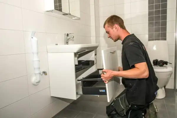 En man installerar en vit kommod i ett kaklat badrum.