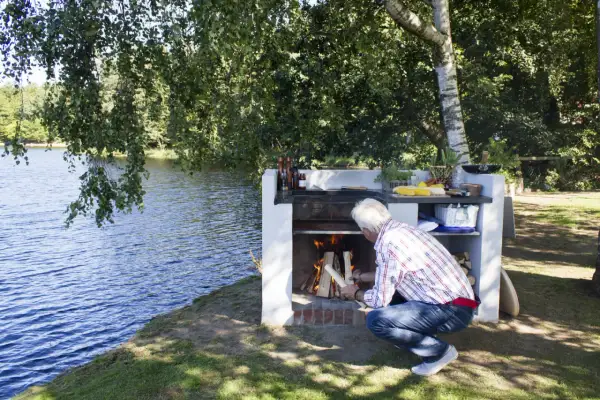 Man tänder en brasa vid en murad grillplats vid en sjö.